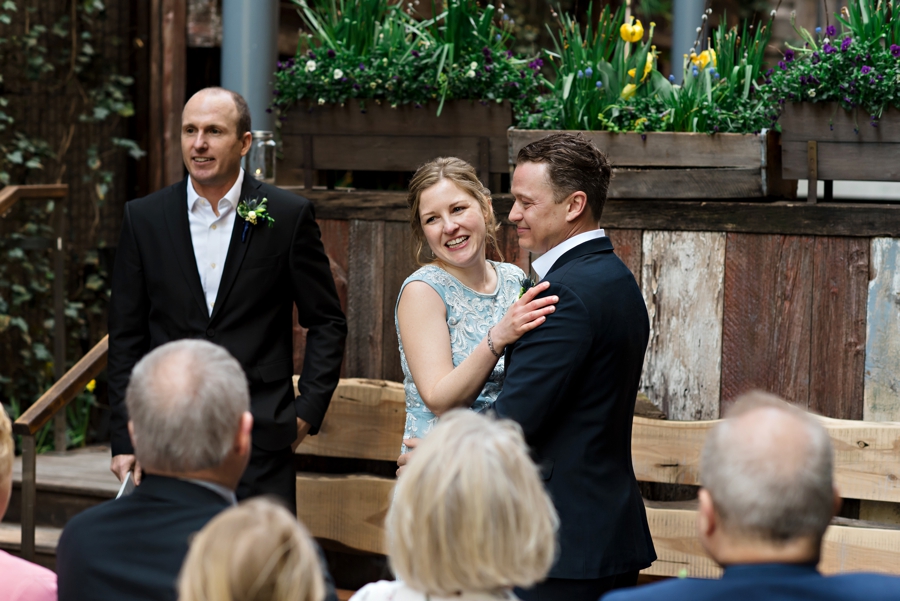 A newly married couple laugh and hug in front of their wedding guests.